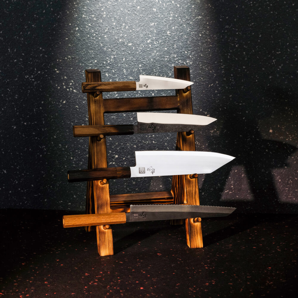 RAW OAK knife set with four kitchen knives on a wooden knife stand against a dark background.
