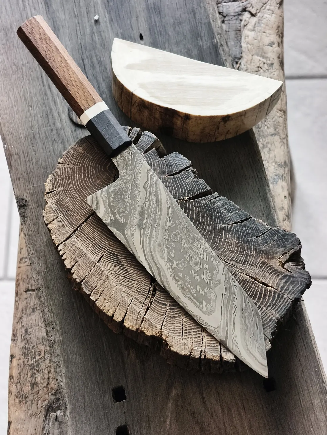 One of Jacob Bech's custom knives with a Damascus blade, on a slice of oak