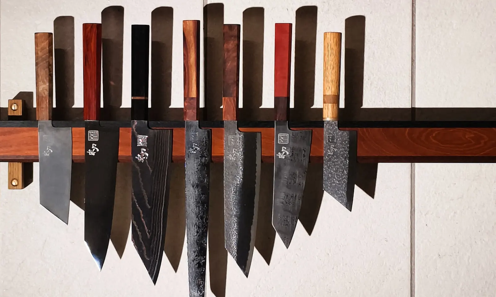 Seven custom knives with different handles on a wall rack